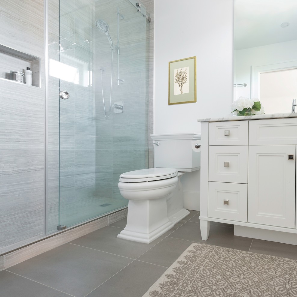 Photo of a traditional master bathroom in Vancouver with recessed-panel cabinets, white cabinets, a two-piece toilet, gray tile, limestone, white walls, porcelain floors, an undermount sink, marble benchtops, grey floor and white benchtops.
