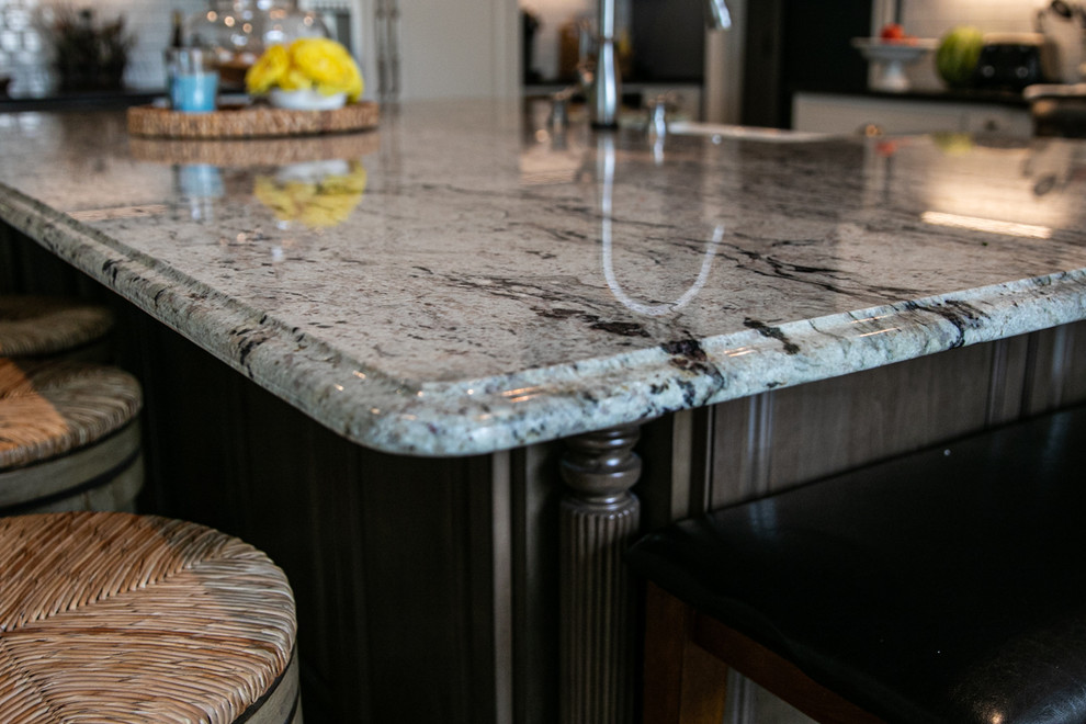 Large transitional l-shaped medium tone wood floor and brown floor open concept kitchen photo in Charlotte with a farmhouse sink, white cabinets, granite countertops, white backsplash, stainless steel appliances, an island, raised-panel cabinets, porcelain backsplash and white countertops