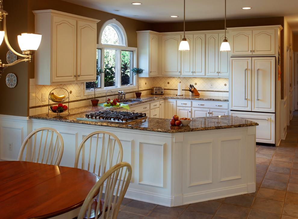Photo of a large traditional u-shaped eat-in kitchen in Philadelphia with a double-bowl sink, raised-panel cabinets, white cabinets, granite benchtops, white splashback, porcelain splashback, panelled appliances, ceramic floors, a peninsula and brown floor.
