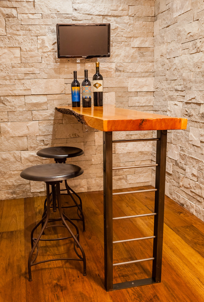 This is an example of a mid-sized transitional u-shaped seated home bar in St Louis with an undermount sink, solid surface benchtops, multi-coloured splashback and medium hardwood floors.