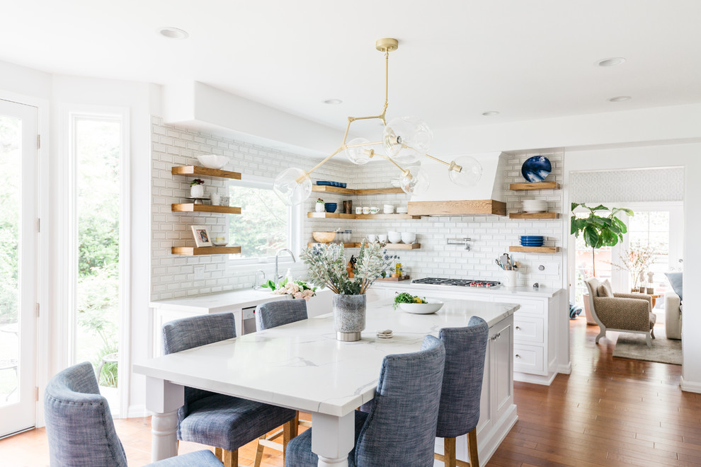 Inspiration for a mid-sized transitional u-shaped medium tone wood floor and brown floor eat-in kitchen remodel in Los Angeles with a farmhouse sink, recessed-panel cabinets, white cabinets, quartzite countertops, white backsplash, subway tile backsplash, stainless steel appliances, an island and white countertops