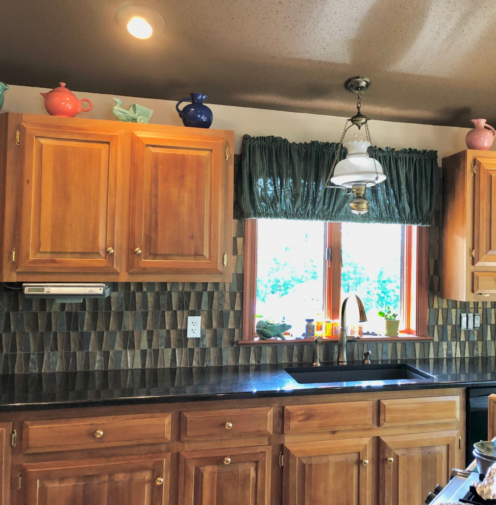 Example of a mid-sized arts and crafts l-shaped eat-in kitchen design with an undermount sink, raised-panel cabinets, medium tone wood cabinets, granite countertops, multicolored backsplash, glass tile backsplash, an island and black countertops