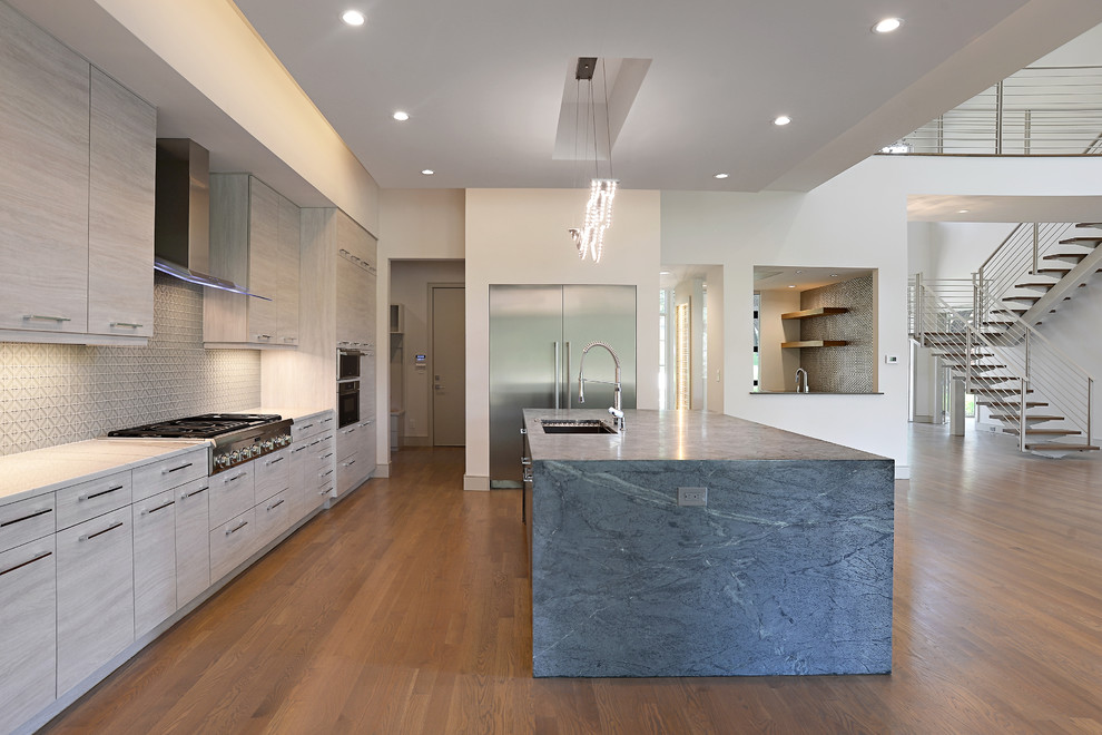 Large contemporary l-shaped open plan kitchen in Dallas with flat-panel cabinets, grey cabinets, concrete benchtops, grey splashback, stainless steel appliances, light hardwood floors, with island and brown floor.