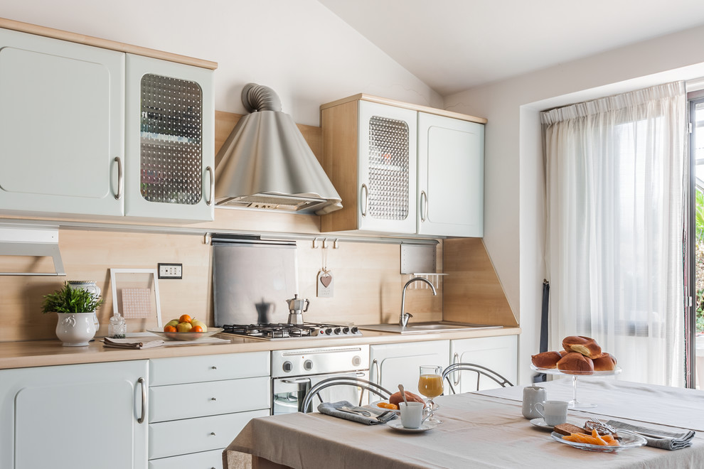 This is an example of a country single-wall eat-in kitchen in Other with an integrated sink, recessed-panel cabinets, blue cabinets, wood benchtops, beige splashback, timber splashback, stainless steel appliances and no island.