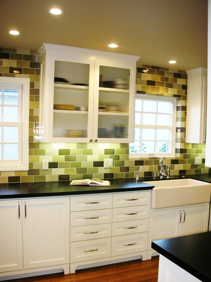This is an example of a small traditional galley separate kitchen in Sacramento with subway tile splashback, a farmhouse sink, shaker cabinets, white cabinets, solid surface benchtops, green splashback, stainless steel appliances and medium hardwood floors.
