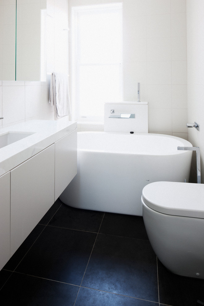 This is an example of a small contemporary bathroom in Sydney with an undermount sink, white cabinets, marble benchtops, a freestanding tub, an open shower, a wall-mount toilet, white tile, porcelain tile, white walls and porcelain floors.