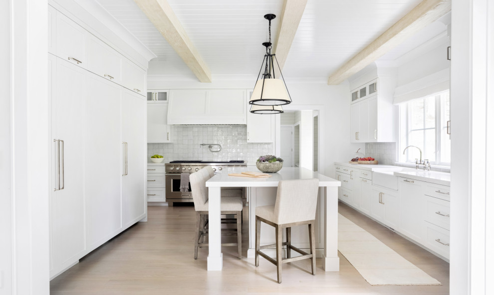 Design ideas for a large traditional l-shaped eat-in kitchen in New York with a farmhouse sink, recessed-panel cabinets, white cabinets, marble benchtops, white splashback, terra-cotta splashback, stainless steel appliances, light hardwood floors, with island, brown floor and white benchtop.