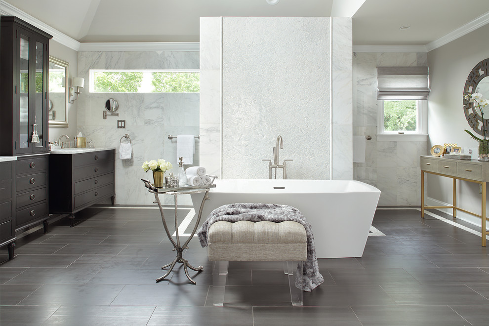 Photo of an expansive transitional master bathroom in New York with furniture-like cabinets, black cabinets, a freestanding tub, a double shower, a two-piece toilet, gray tile, marble, grey walls, porcelain floors, an integrated sink, marble benchtops, grey floor and a hinged shower door.
