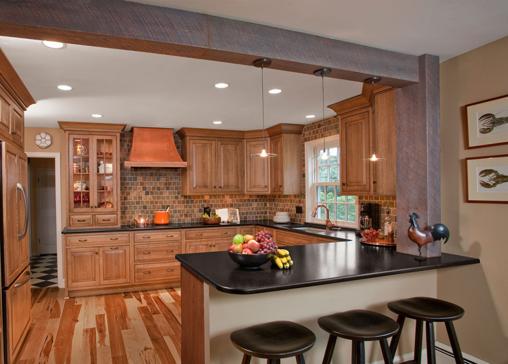 This is an example of a large country u-shaped eat-in kitchen in Cleveland with an undermount sink, raised-panel cabinets, brown cabinets, onyx benchtops, multi-coloured splashback, ceramic splashback, stainless steel appliances, light hardwood floors, with island, brown floor and black benchtop.