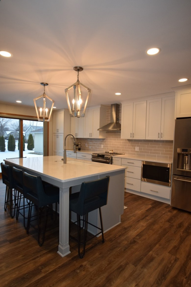 Kitchen - transitional galley vinyl floor and brown floor kitchen idea with an undermount sink, shaker cabinets, white cabinets, quartz countertops, beige backsplash, subway tile backsplash, stainless steel appliances, an island and white countertops