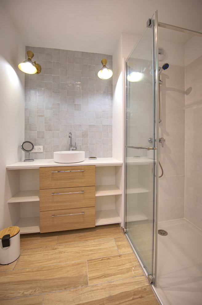 This is an example of a small beach style 3/4 bathroom in Montpellier with wood-look tile, a drop-in sink, white benchtops, a single vanity, beaded inset cabinets, light wood cabinets, gray tile, terra-cotta tile, white walls, beige floor, a freestanding vanity, a two-piece toilet and a sliding shower screen.