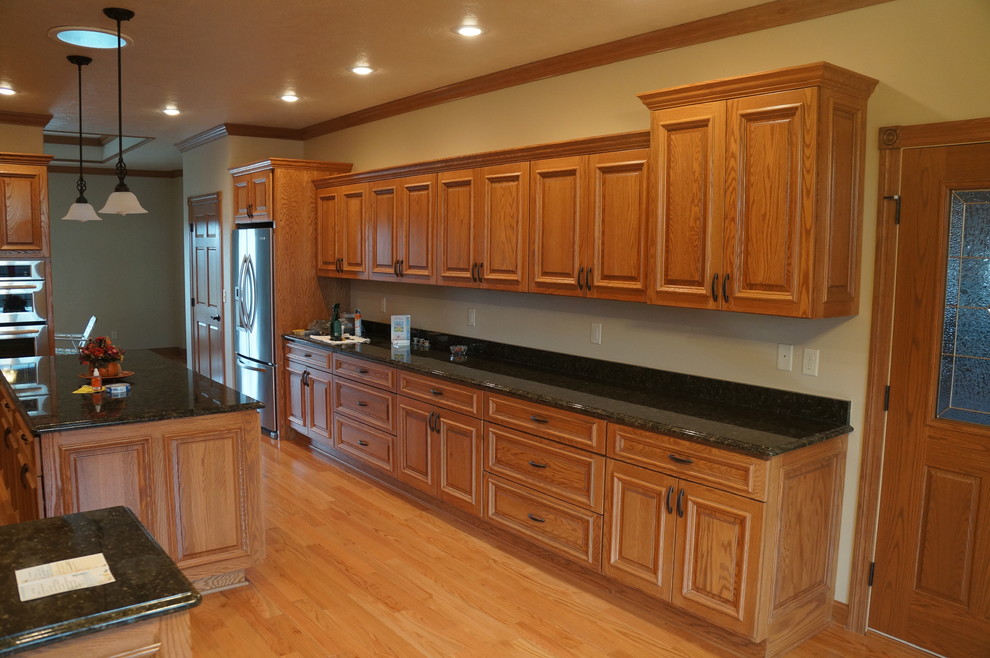 This is an example of a large traditional galley eat-in kitchen in Other with raised-panel cabinets, medium wood cabinets, stainless steel appliances, light hardwood floors and with island.