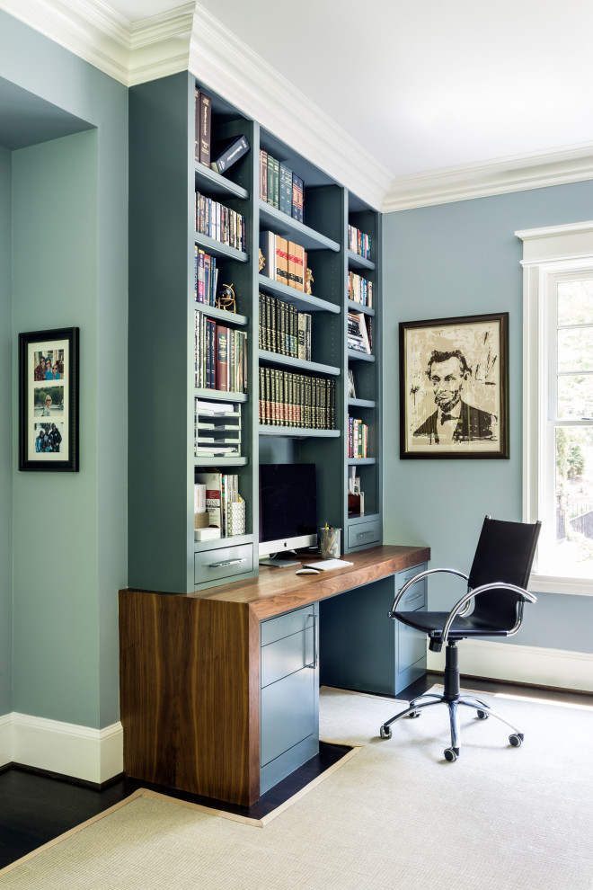 This is an example of a transitional home office in DC Metro with a library, a built-in desk, blue walls, dark hardwood floors and brown floor.