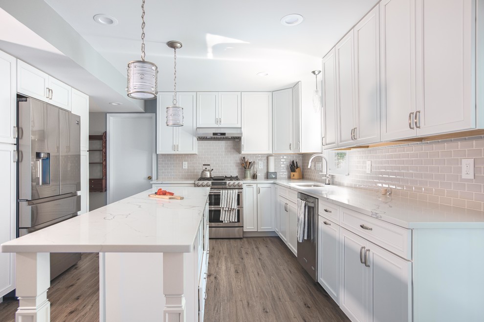 Design ideas for a large contemporary u-shaped open plan kitchen in DC Metro with an undermount sink, raised-panel cabinets, white cabinets, quartz benchtops, grey splashback, subway tile splashback, stainless steel appliances, vinyl floors, with island, brown floor and white benchtop.
