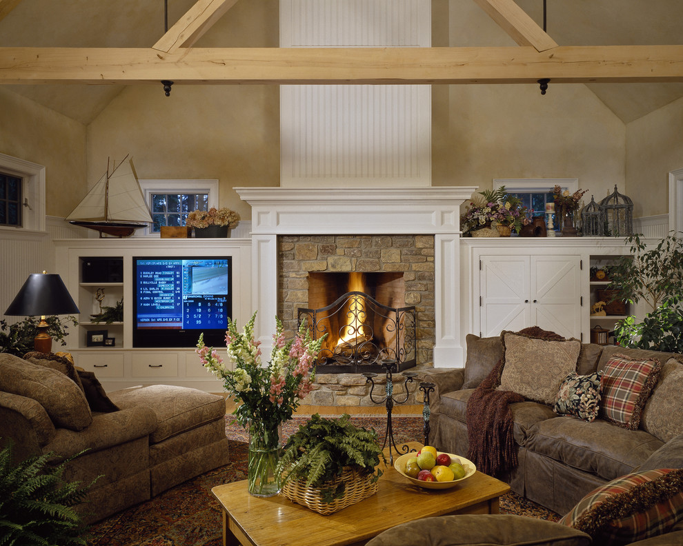 This is an example of a country family room in New York with beige walls, a standard fireplace, a stone fireplace surround and a built-in media wall.