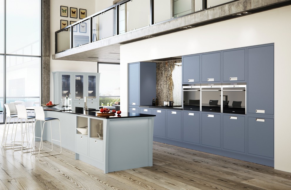 This is an example of a transitional kitchen in West Midlands with an undermount sink, flat-panel cabinets, blue cabinets, black appliances, light hardwood floors and with island.