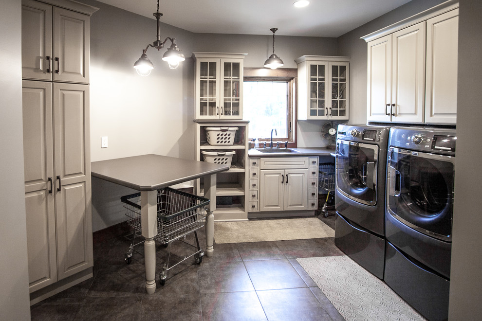 Photo of a mid-sized arts and crafts l-shaped laundry room in Other with raised-panel cabinets, solid surface benchtops, grey walls, vinyl floors, a side-by-side washer and dryer and white cabinets.
