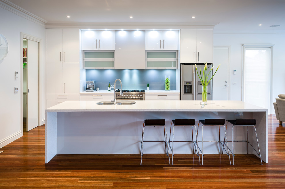Contemporary kitchen in Melbourne with a double-bowl sink, flat-panel cabinets, white cabinets, stainless steel appliances, medium hardwood floors and with island.