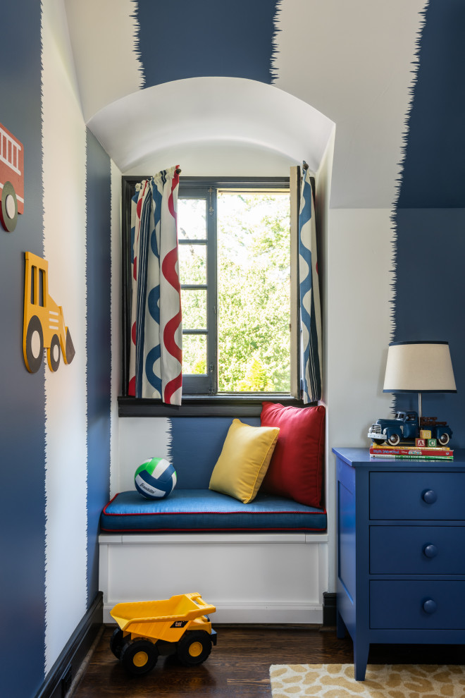Boy's Bedroom - A long-term client was expecting her third child. Alas, this meant that baby number two was getting booted from the coveted nursery as his sister before him had. The most convenient room in the house for the son, was dad’s home office, and dad would be relocated into the garage carriage house.
For the new bedroom, mom requested a bold, colorful space with a truck theme.
The existing office had no door and was located at the end of a long dark hallway that had been painted black by the last homeowners. First order of business was to lighten the hall and create a wall space for functioning doors. The awkward architecture of the room with 3 alcove windows, slanted ceilings and built-in bookcases proved an inconvenient location for furniture placement. We opted to place the bed close the wall so the two-year-old wouldn’t fall out. The solid wood bed and nightstand were constructed in the US and painted in vibrant shades to match the bedding and roman shades. The amazing irregular wall stripes were inherited from the previous homeowner but were also black and proved too dark for a toddler. Both myself and the client loved them and decided to have them re-painted in a daring blue. The daring fabric used on the windows counter- balance the wall stripes.
Window seats and a built-in toy storage were constructed to make use of the alcove windows. Now, the room is not only fun and bright, but functional.