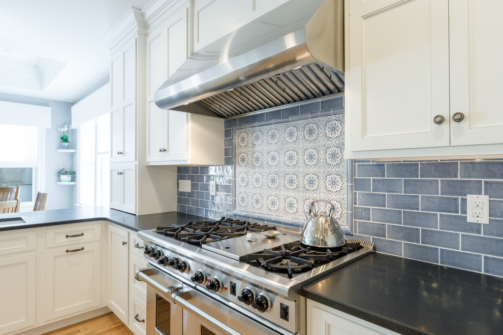 This is an example of a large traditional kitchen in Other with an undermount sink, shaker cabinets, white cabinets, granite benchtops, blue splashback, glass tile splashback, stainless steel appliances, light hardwood floors, with island and black benchtop.