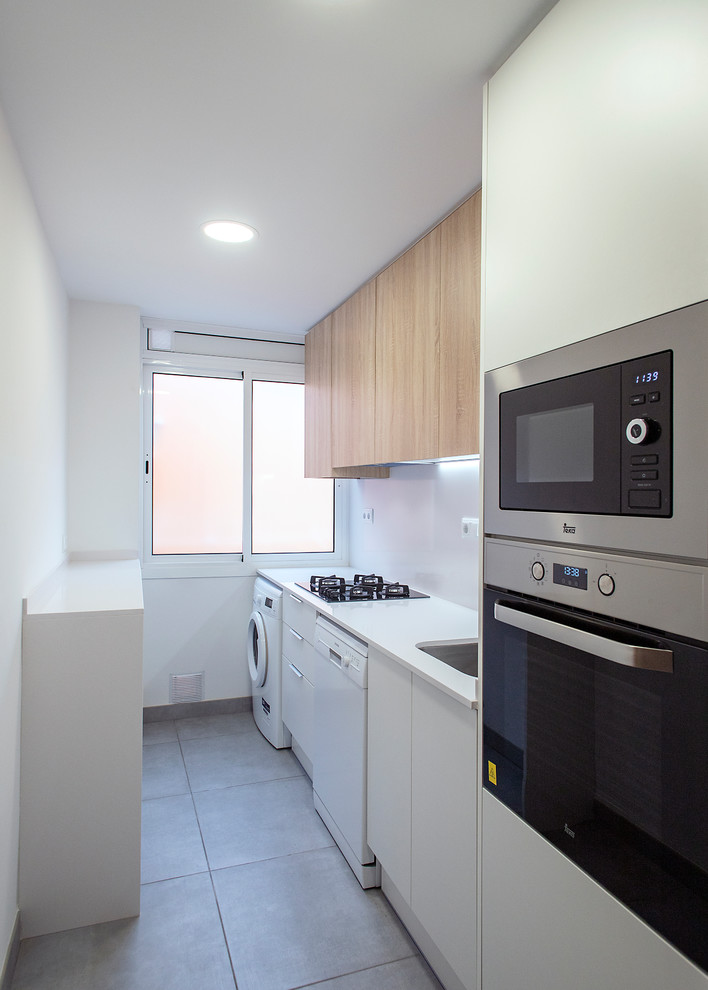 Photo of a mid-sized contemporary single-wall separate kitchen in Barcelona with a single-bowl sink, flat-panel cabinets, white cabinets, white splashback, stainless steel appliances, no island, grey floor and white benchtop.