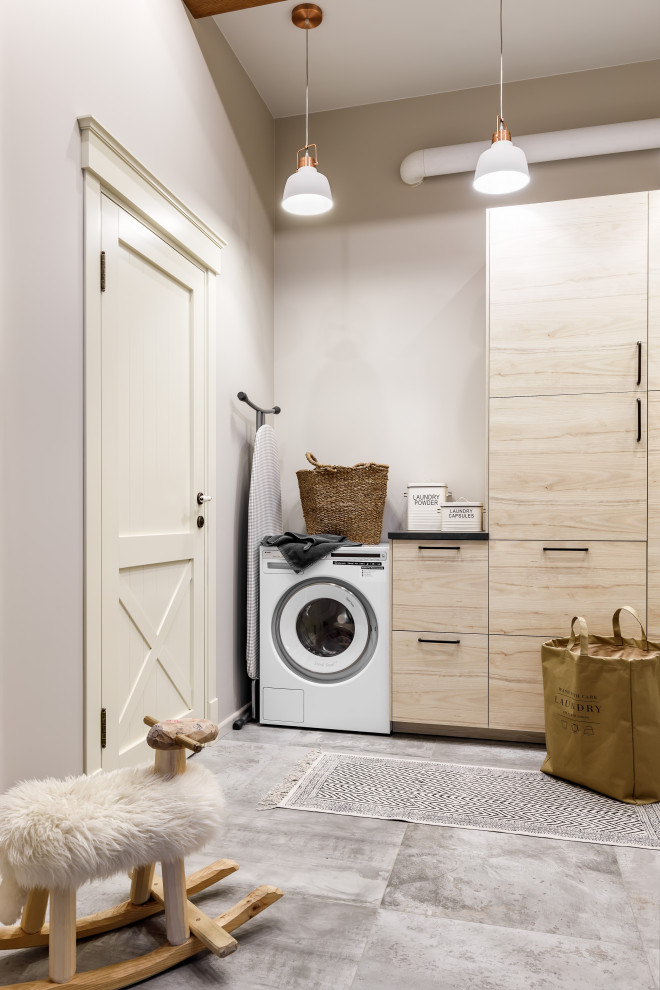Mid-sized country single-wall dedicated laundry room in Saint Petersburg with flat-panel cabinets, beige cabinets, solid surface benchtops, beige walls, porcelain floors, a side-by-side washer and dryer, grey floor and black benchtop.