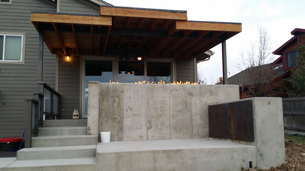 This is an example of a mid-sized industrial backyard patio in Denver with a fire feature, concrete slab and a roof extension.