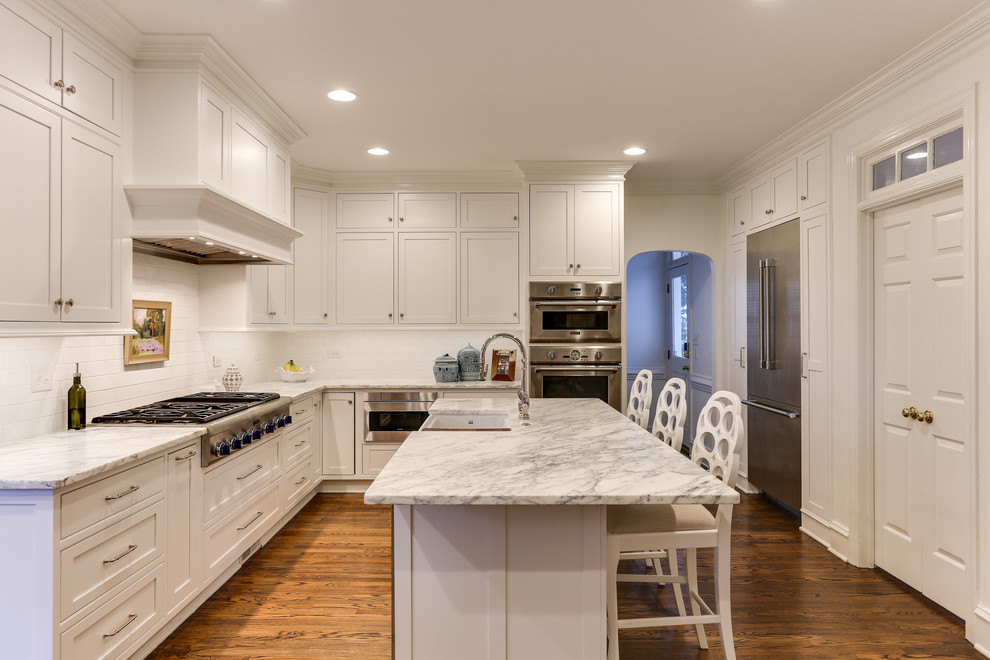 Inspiration for a mid-sized traditional l-shaped separate kitchen in Raleigh with a farmhouse sink, beaded inset cabinets, white cabinets, marble benchtops, white splashback, ceramic splashback, stainless steel appliances, medium hardwood floors, with island, brown floor and white benchtop.