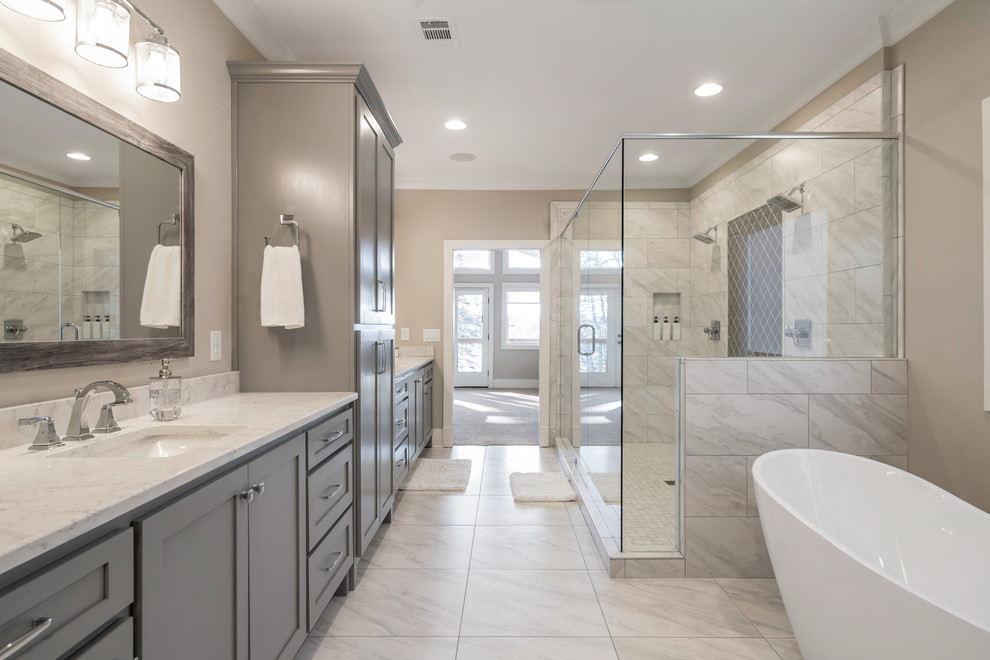 Photo of a mid-sized arts and crafts master bathroom in Other with recessed-panel cabinets, grey cabinets, a freestanding tub, an alcove shower, a two-piece toilet, gray tile, marble, beige walls, marble floors, an undermount sink, engineered quartz benchtops, white floor, a hinged shower door and white benchtops.