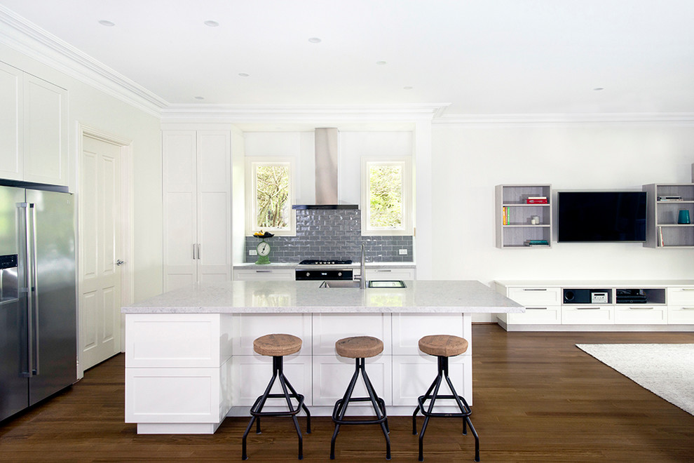 Inspiration for a large transitional l-shaped open plan kitchen in Melbourne with a double-bowl sink, shaker cabinets, white cabinets, quartz benchtops, grey splashback, subway tile splashback, stainless steel appliances, medium hardwood floors, with island, brown floor and grey benchtop.