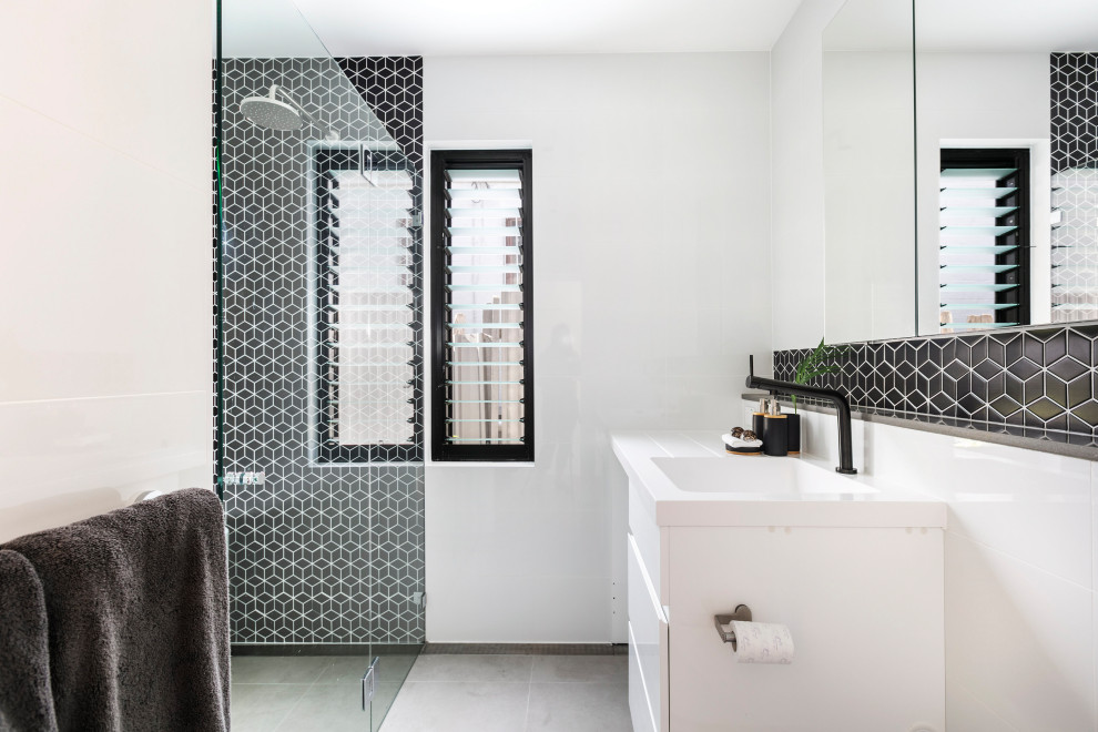 Источник вдохновения для домашнего уюта: маленькая ванная комната в стиле модернизм с фасадами с филенкой типа жалюзи, белыми фасадами, ванной в нише, душевой комнатой, унитазом-моноблоком, черно-белой плиткой, плиткой мозаикой, белыми стенами, полом из цементной плитки, душевой кабиной, подвесной раковиной, столешницей из искусственного кварца, серым полом, душем с распашными дверями, белой столешницей, тумбой под одну раковину и подвесной тумбой для на участке и в саду