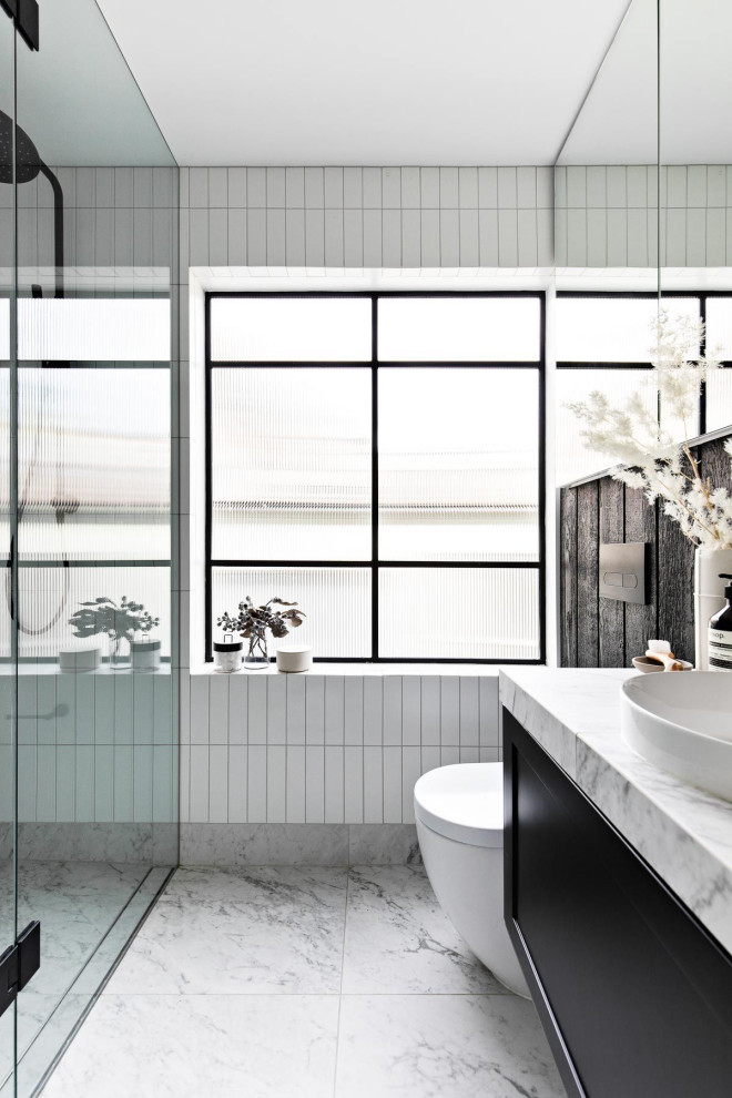 Idée de décoration pour une salle de bain urbaine avec des portes de placard noires, une douche double, un carrelage blanc, un sol en marbre, un plan de toilette en carrelage, une niche, meuble simple vasque, boiseries et des carreaux de céramique.