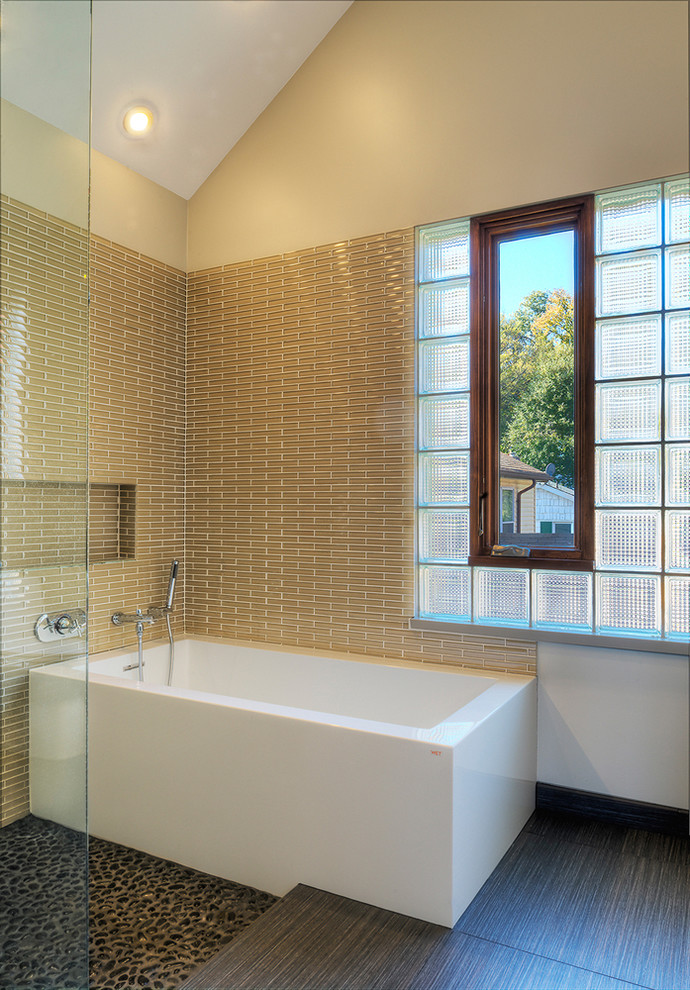 This is an example of a mid-sized modern master bathroom in DC Metro with a freestanding tub, beige tile, matchstick tile, pebble tile floors, a one-piece toilet and beige walls.