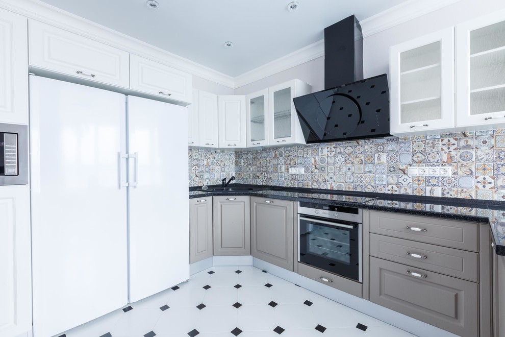 Example of a mid-sized trendy u-shaped white floor open concept kitchen design with an undermount sink, glass-front cabinets, white cabinets, multicolored backsplash, ceramic backsplash, stainless steel appliances, a peninsula and black countertops