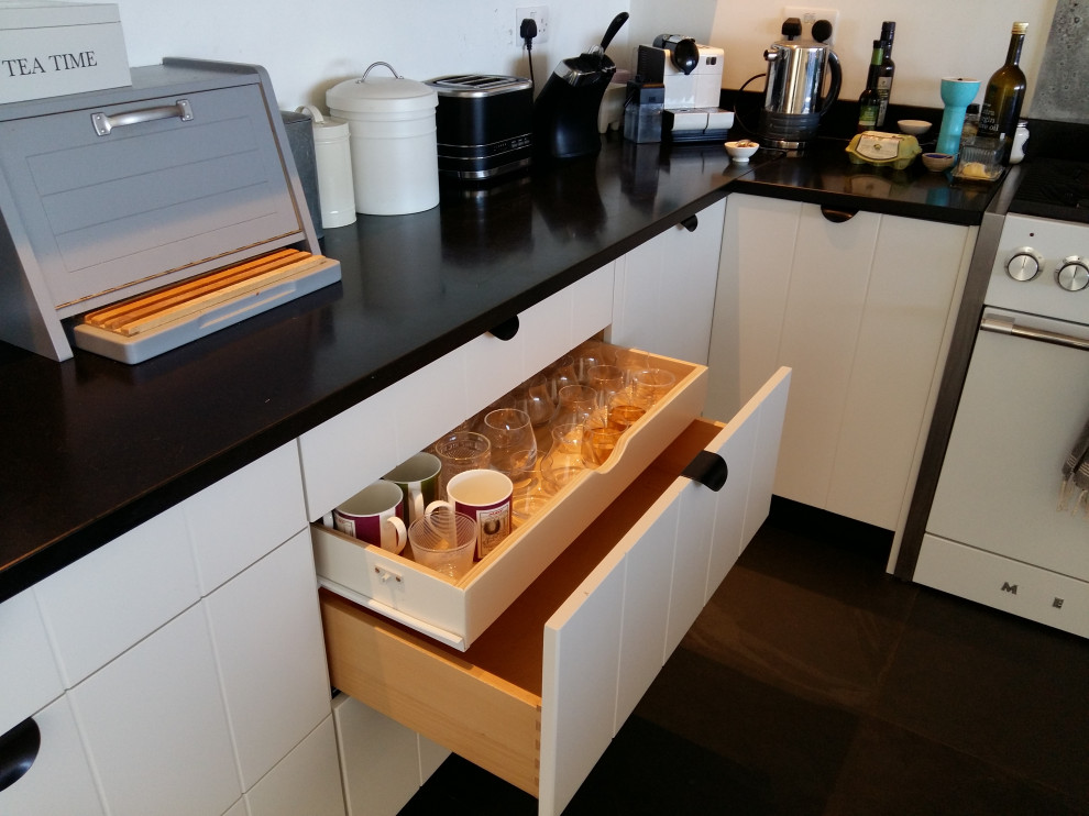 Large beach style u-shaped eat-in kitchen in Cornwall with a double-bowl sink, flat-panel cabinets, white cabinets, granite benchtops, multi-coloured splashback, slate floors, grey floor and black benchtop.
