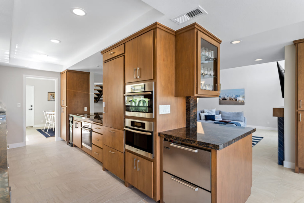 This is an example of a large transitional galley open plan kitchen in Los Angeles with a double-bowl sink, glass-front cabinets, brown cabinets, quartz benchtops, multi-coloured splashback, engineered quartz splashback, stainless steel appliances, porcelain floors, no island, beige floor and multi-coloured benchtop.