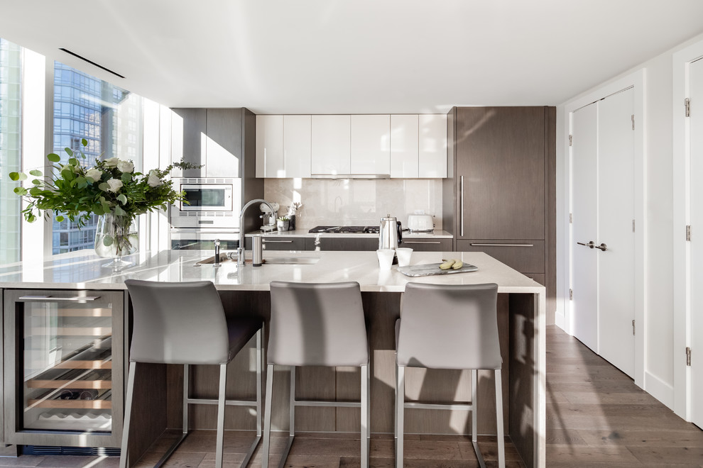 This is an example of a mid-sized contemporary galley kitchen in Vancouver with an undermount sink, flat-panel cabinets, dark wood cabinets, quartz benchtops, beige splashback, stainless steel appliances, with island, grey floor, beige benchtop, stone slab splashback and dark hardwood floors.
