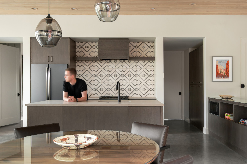 Photo of a modern open plan kitchen in Salt Lake City with a submerged sink, flat-panel cabinets, medium wood cabinets, engineered stone countertops, multi-coloured splashback, cement tile splashback, black appliances, concrete flooring, an island, grey floors, grey worktops and a wood ceiling.