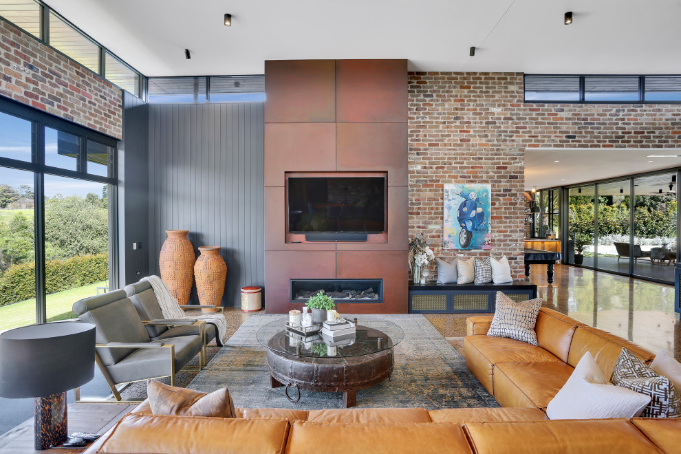 Пример оригинального дизайна: огромная открытая гостиная комната в современном стиле с коричневыми стенами, бетонным полом, стандартным камином, фасадом камина из металла, телевизором на стене и коричневым полом