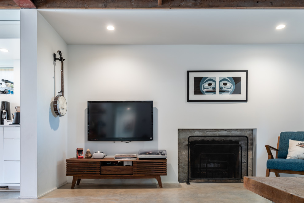 This is an example of a medium sized industrial open plan games room in Vancouver with white walls, concrete flooring, a standard fireplace, a brick fireplace surround and a wall mounted tv.