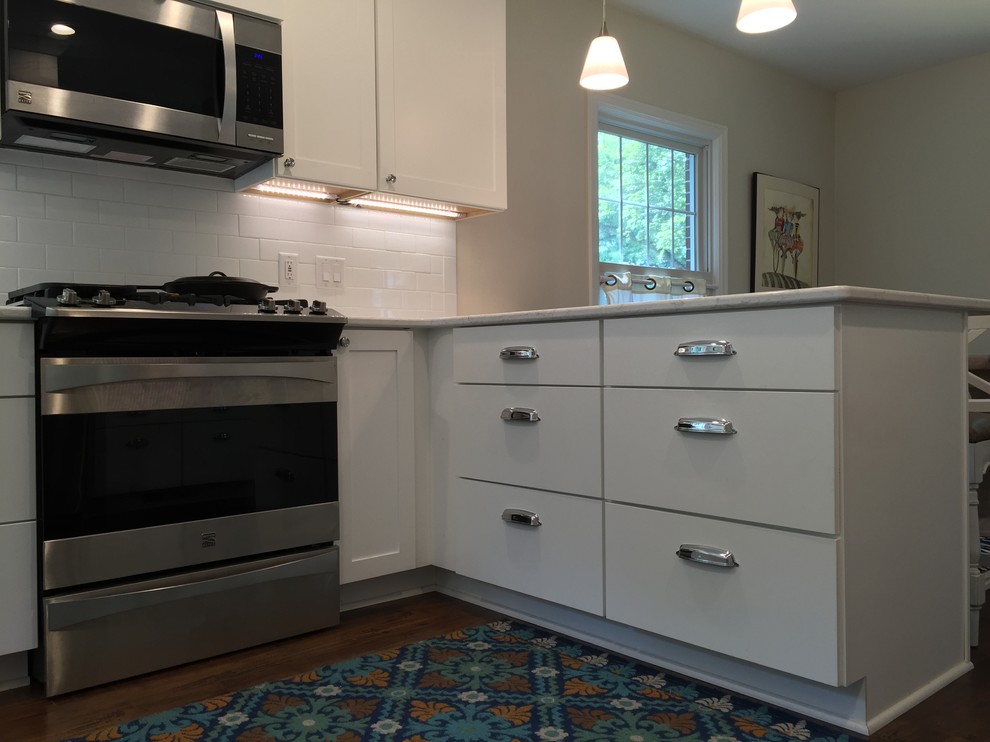 Example of a mid-sized transitional u-shaped eat-in kitchen design in Grand Rapids with flat-panel cabinets, white cabinets, quartz countertops, white backsplash, subway tile backsplash, stainless steel appliances, a peninsula and white countertops