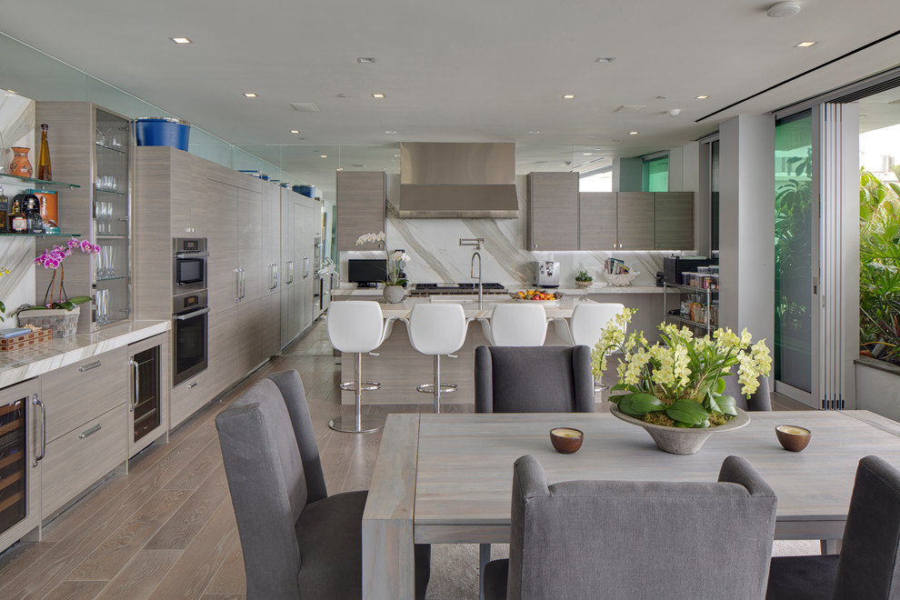 Beach style eat-in kitchen in Los Angeles with flat-panel cabinets, light wood cabinets, marble benchtops, white splashback, marble splashback, stainless steel appliances, light hardwood floors, with island, beige floor and white benchtop.