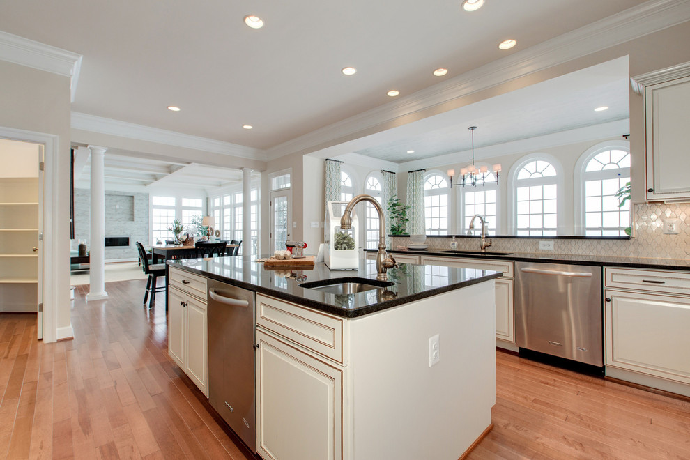 This is an example of a large transitional u-shaped eat-in kitchen in DC Metro with an undermount sink, raised-panel cabinets, white cabinets, granite benchtops, beige splashback, stone tile splashback, stainless steel appliances, vinyl floors and with island.