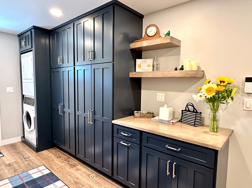 Mid-sized transitional single-wall medium tone wood floor and beige floor utility room photo with recessed-panel cabinets, blue cabinets, wood countertops, white walls, a stacked washer/dryer and beige countertops