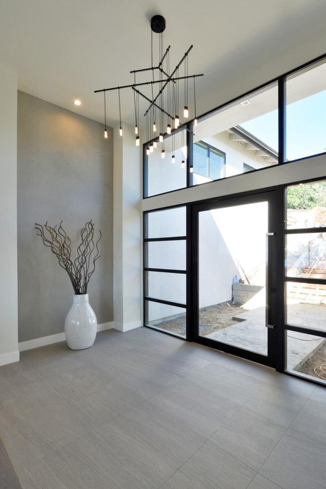 This is an example of an expansive modern foyer in San Diego with white walls, a pivot front door, a glass front door and porcelain floors.