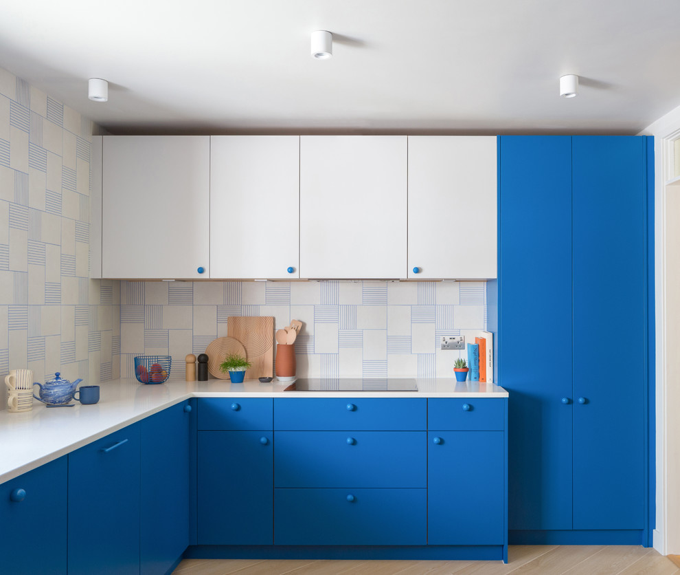 This is an example of a mid-sized contemporary l-shaped kitchen in Cambridgeshire with flat-panel cabinets, blue cabinets, solid surface benchtops, white splashback, porcelain splashback, porcelain floors, no island, beige floor and white benchtop.