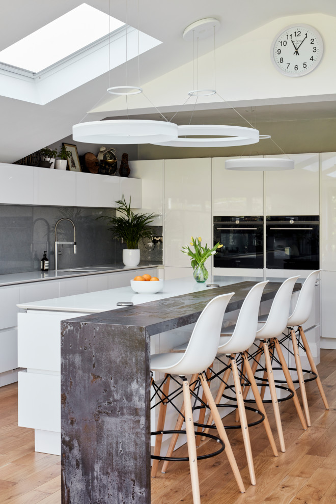 Photo of a large modern galley kitchen/diner in London with a built-in sink, flat-panel cabinets, white cabinets, granite worktops, grey splashback, metal splashback, integrated appliances, dark hardwood flooring, an island, brown floors and white worktops.