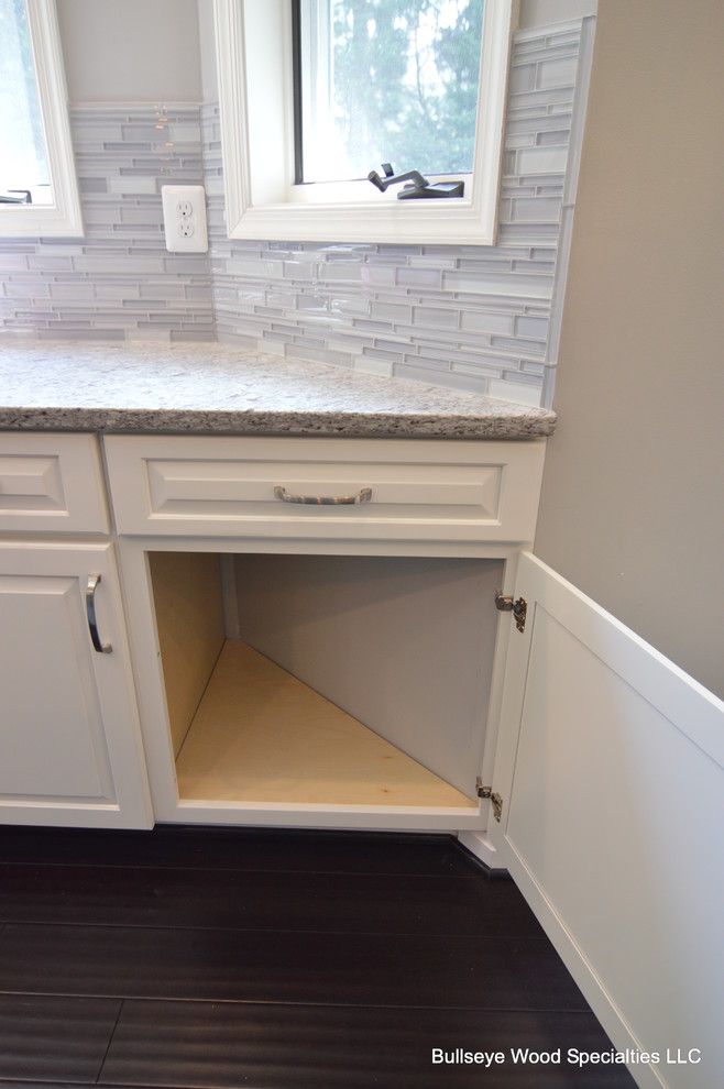 Example of a large transitional u-shaped dark wood floor and brown floor eat-in kitchen design in DC Metro with an undermount sink, raised-panel cabinets, white cabinets, granite countertops, gray backsplash, glass tile backsplash, stainless steel appliances and an island