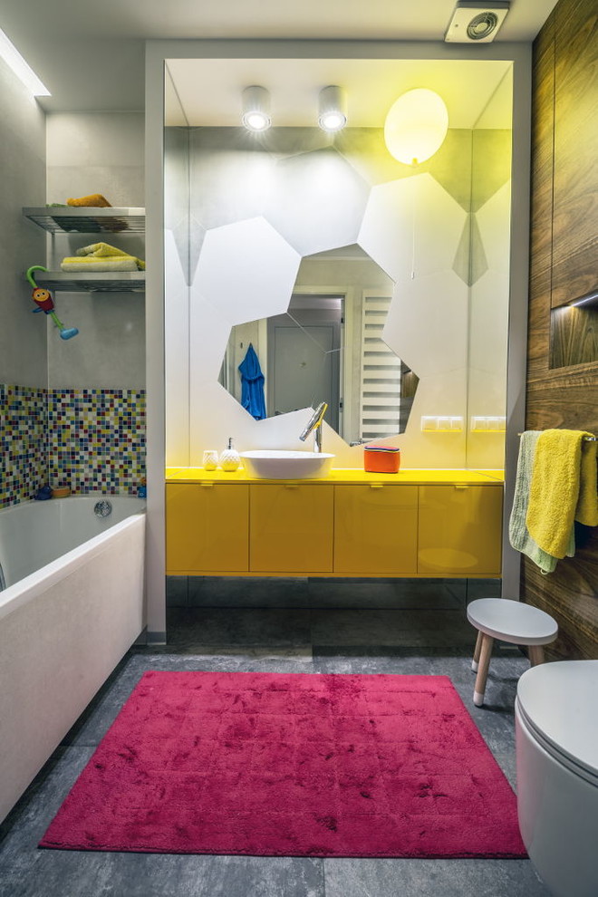 This is an example of a mid-sized eclectic kids bathroom in Other with yellow cabinets, a corner tub, a corner shower, ceramic tile, porcelain floors, grey floor, a sliding shower screen, yellow benchtops, flat-panel cabinets, a wall-mount toilet, multi-coloured tile, multi-coloured walls and a vessel sink.