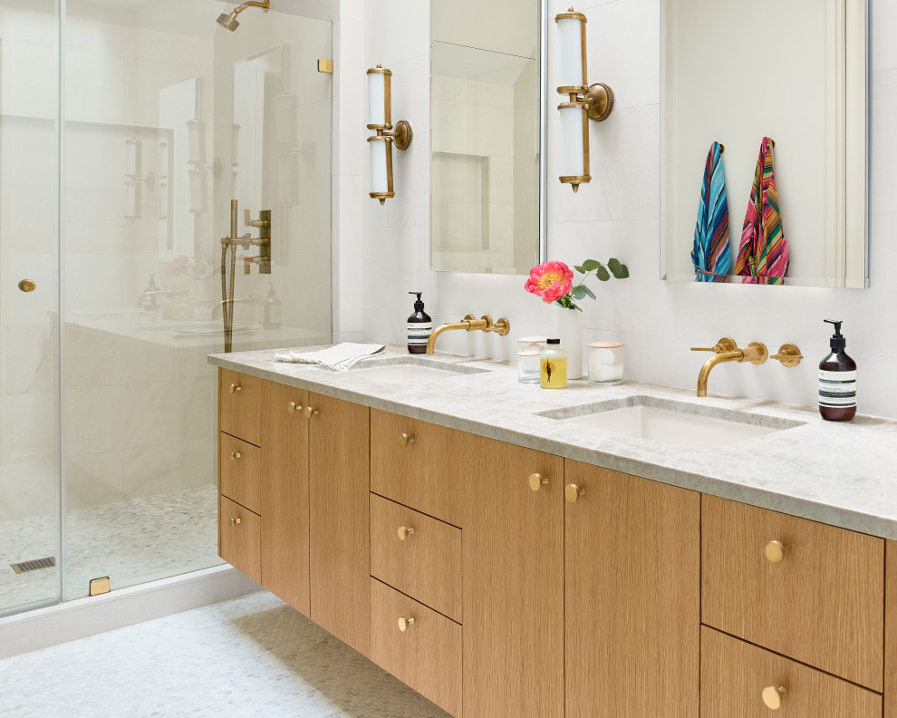 This is an example of a mid-sized contemporary master bathroom in Austin with flat-panel cabinets, light wood cabinets, a curbless shower, white tile, ceramic tile, white walls, mosaic tile floors, a drop-in sink, marble benchtops, white floor, a hinged shower door, beige benchtops, a double vanity and a built-in vanity.